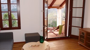 Una habitación con piso de madera, un sofá gris, una mesita redonda con una jarra verde y vistas a un balcón con una silla y una mesa.