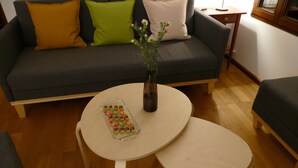 Una sala de estar con un sofá gris, una mesita redonda con un florero y una bandeja de aperitivos.