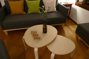 Una sala de estar con un sofá gris, una mesita redonda con un florero y una bandeja de aperitivos.