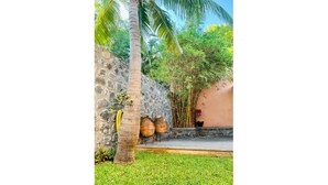 A stone wall with a palm tree, a bamboo plant, and a small garden area with a wooden deck. - Bungalow for 2 - Ocean View (Saint Paul)