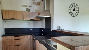 Eine kleine Küche mit Holzausstattung, einer schwarzen Arbeitsplatte, einem Edelstahlspülbecken und einer an der Wand montierten Uhr.