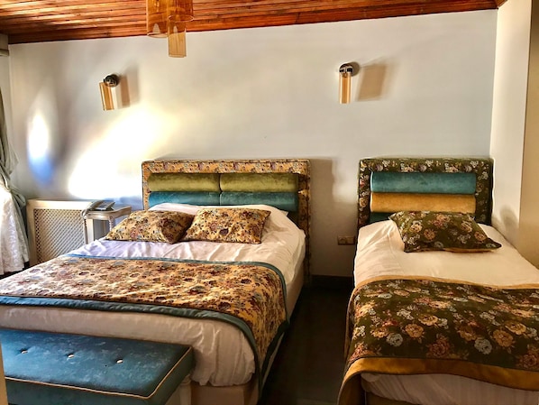Una habitación con dos camas, cada una con ropa de cama y cabeceros estampados. Hay mesitas de noche con lámparas y un ventanal que deja entrar luz natural.