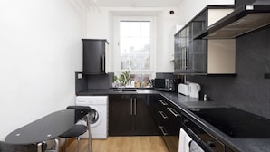 A compact kitchen with a washing machine, a sink, a microwave, and a small dining area with stools.