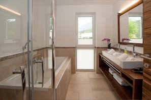 Un baño moderno con cabina de ducha de vidrio, una bañera independiente, un tocador con un espejo grande y vistas al exterior a través de una puerta.