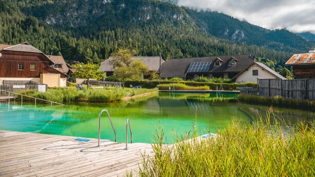 A wooden deck with a swimming pool, surrounded by houses and mountains. - EuroParcs Hermagor  Nassfeld (Hermagor-Pressegger See)