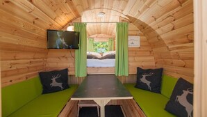 A cozy, wooden cabin room with a bed, green curtains, and a television on the wall. - EuroParcs Hermagor  Nassfeld (Hermagor-Pressegger See)