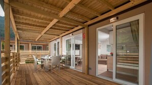 A wooden deck with a table and chairs, glass doors leading to a living area, and a view of a mountain. - EuroParcs Hermagor  Nassfeld (Hermagor-Pressegger See)