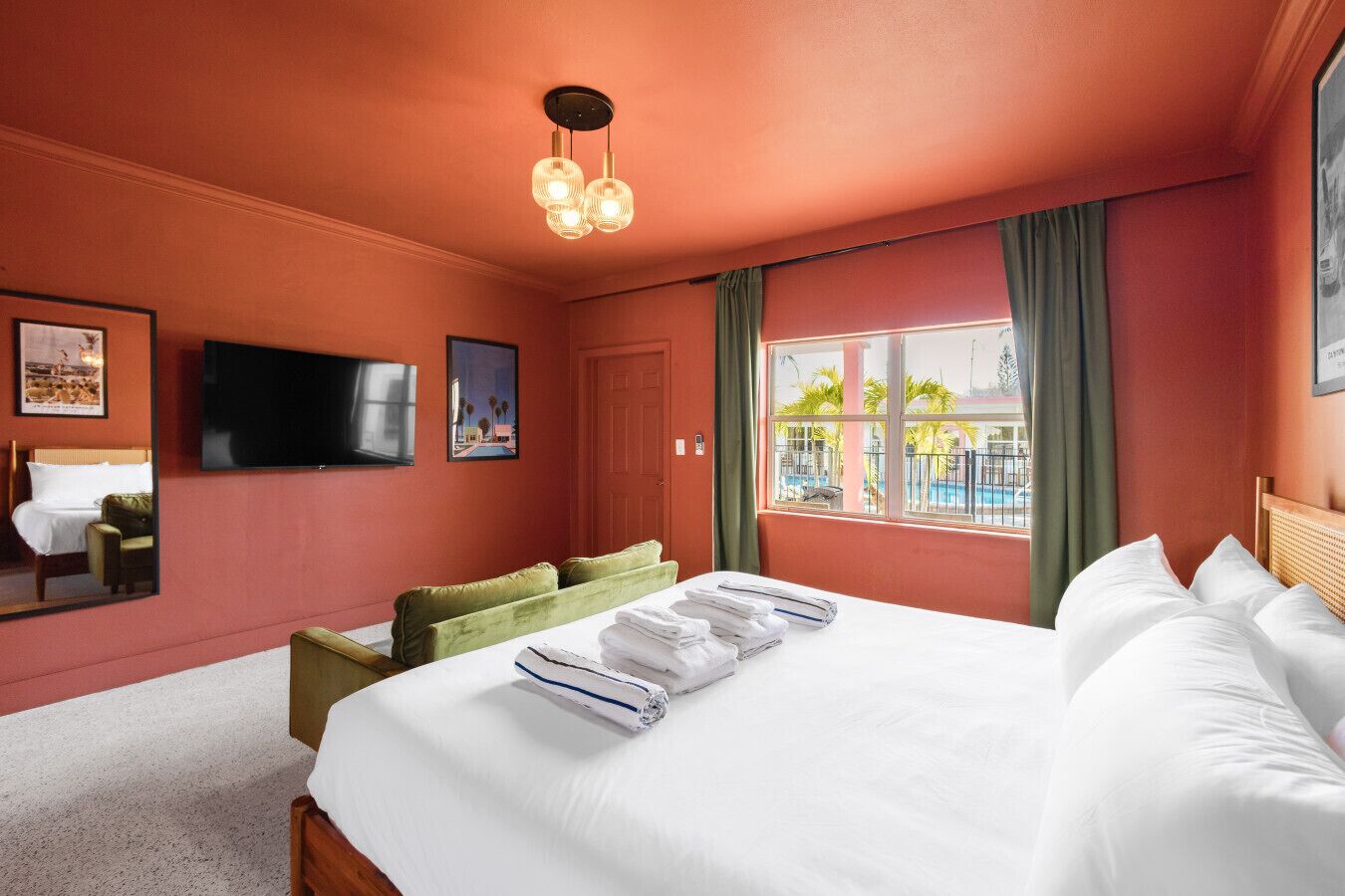 Een hotelkamer met een groot bed, een televisie, een raam met uitzicht op een zwembad en een spiegel.