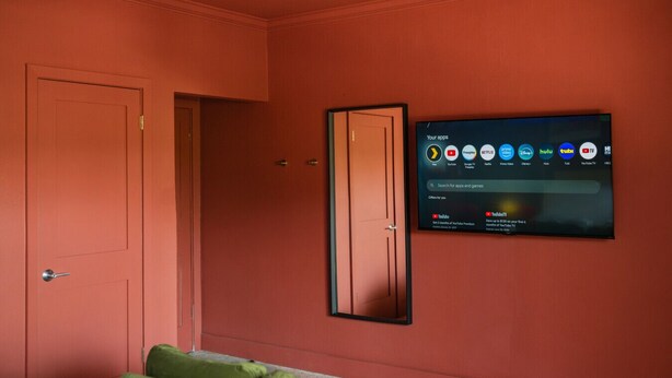 Una habitación con una cama, un sofá verde y un televisor de pared que muestra varias aplicaciones de transmisión.