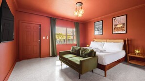 Un dormitorio con cama, un sofá verde, una ventana con cortinas, una puerta y una lámpara fijada a la pared.