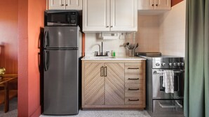 Cocina compacta con refrigerador, microondas, estufa y muebles de madera.