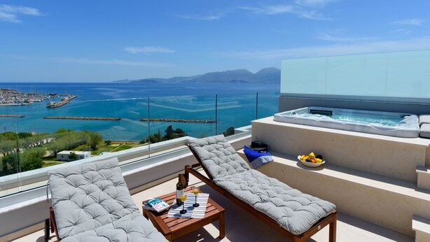 Un balcone con vista sul mare, una vasca idromassaggio, poltroncine da relax e un tavolo con una bottiglia e dei bicchieri.