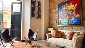 A living room with a stone wall, a sofa, two chairs, a glass coffee table, and a door with shutters. - Apartment in the Heart of Casco Viejo Panama 11 (Panamá)