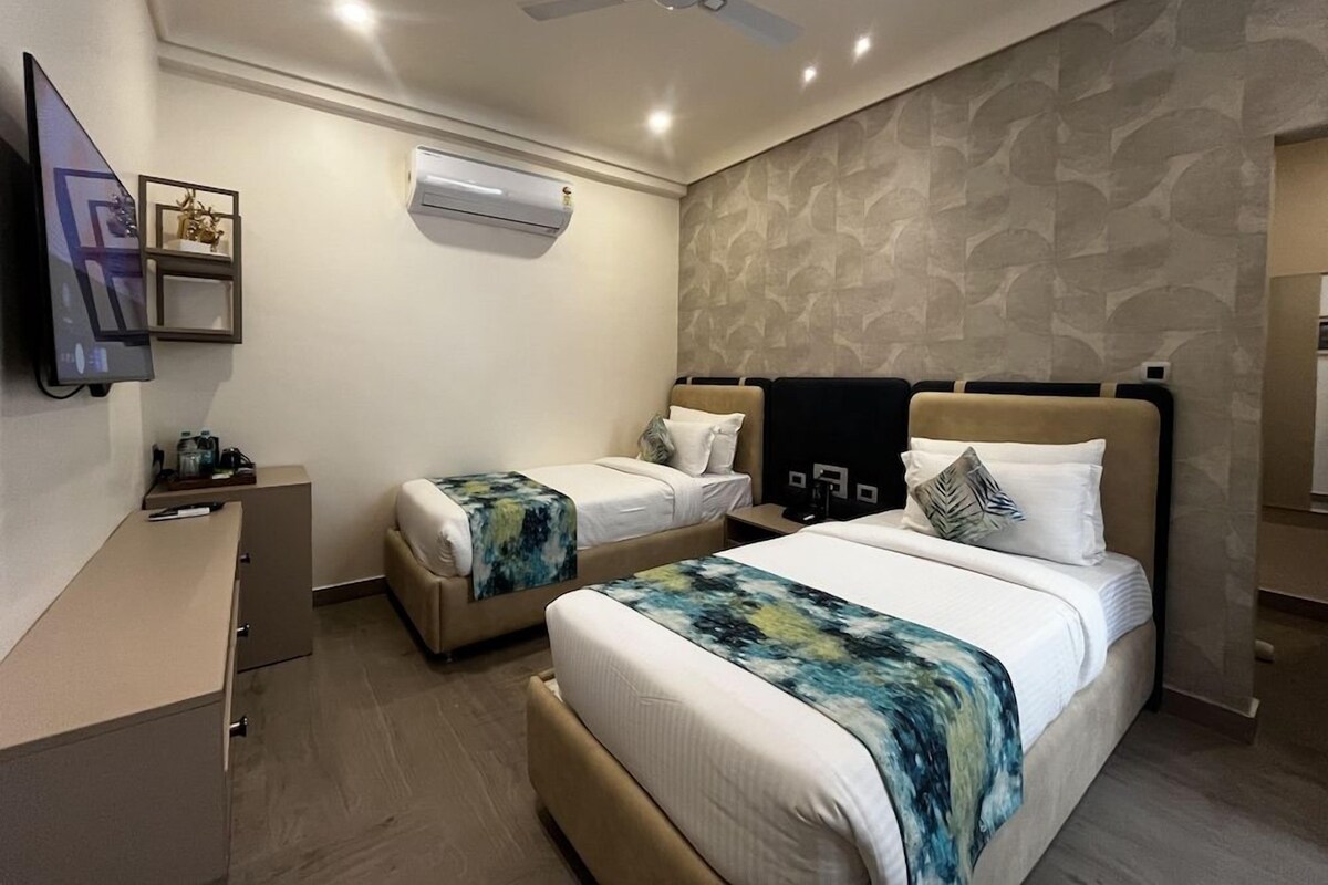 A hotel room with two beds, a desk, a ceiling fan, an air conditioning unit, and a television.