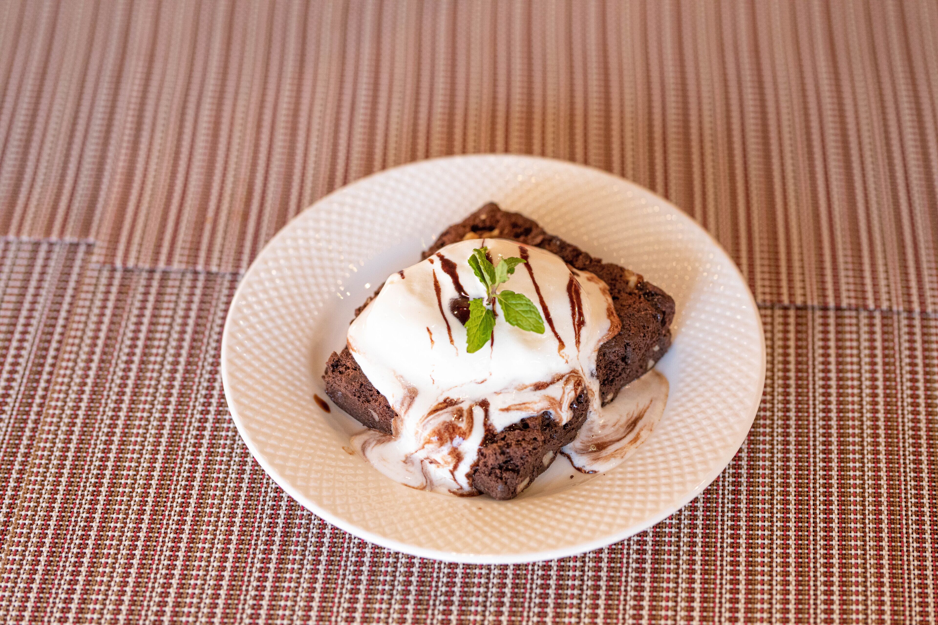 Postre sobre un plato blanco con chocolate y cobertura blanca, sobre un mantel texturizado.