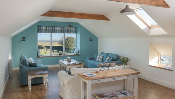 A spacious loft with a high ceiling, exposed wooden beams, a large skylight, and a view of the outdoors.