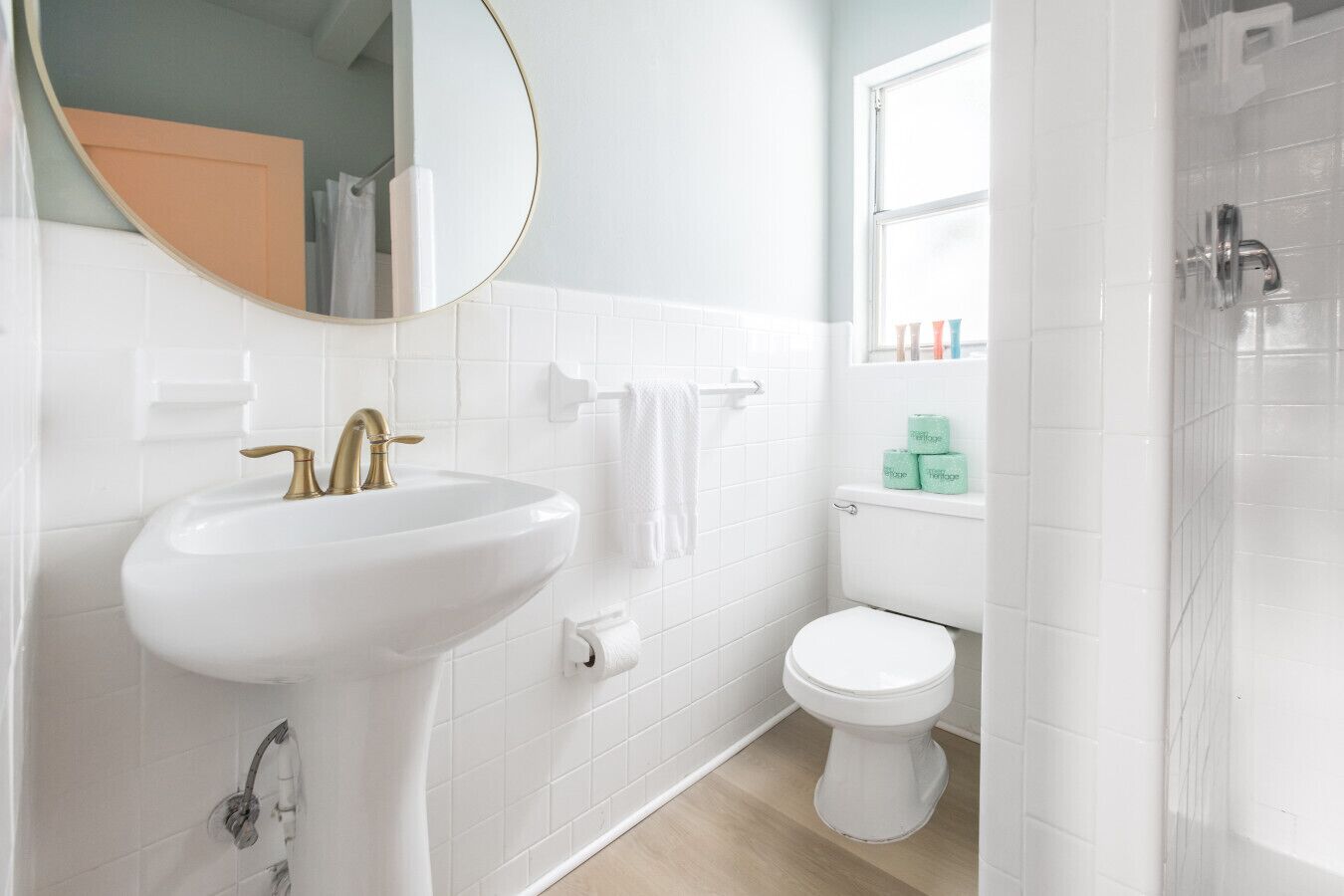 A bathroom with a white sink, gold faucet, white toilet, and a shower area.