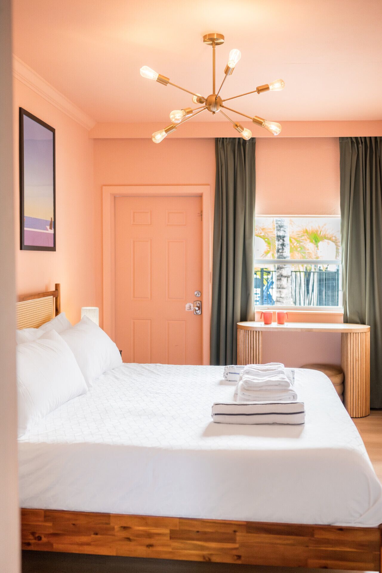 A hotel room with a bed, a window with curtains, a bedside table, and a ceiling light fixture.