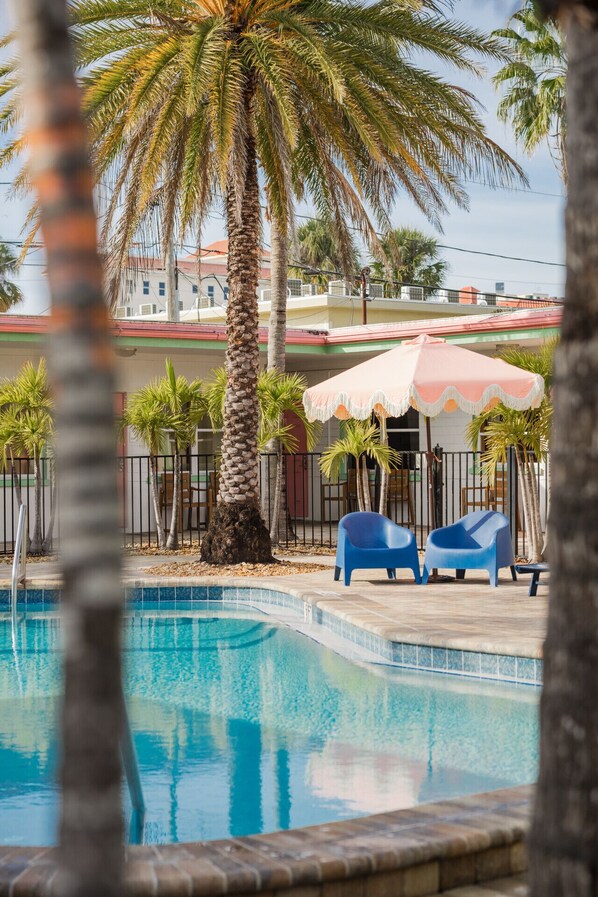 Ein Swimmingpool mit Palmen, einer überdachten Sitzgelegenheit und einem Gebäude im Hintergrund.