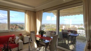 Una sala de estar con un sofá rojo, una mesa de comedor con sillas y un balcón con mesa y sillas.