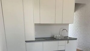 Et kompakt køkken med hvide skabe, en hvid bordplade og et rundt bord med fire hvide stole.