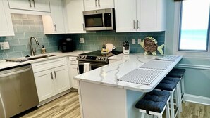 Uma cozinha moderna com armários brancos, uma ilha central com banquetas, micro-ondas de aço inoxidável e lava-louças.