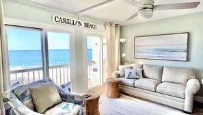 A room with a view of the ocean, a sofa, a chair, and a ceiling fan.