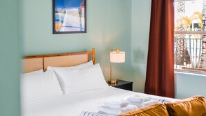 Un cuarto de hotel con cama, mesita de noche, lámpara, ventana con vistas y un cuadro en la pared.