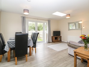 A living room with a dining area, a sofa, a TV on a wooden cabinet, and a large window with curtains.