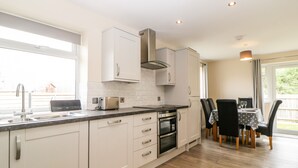 Una cocina moderna con armarios blancos, horno empotrado y zona de comedor con mesa y sillas.