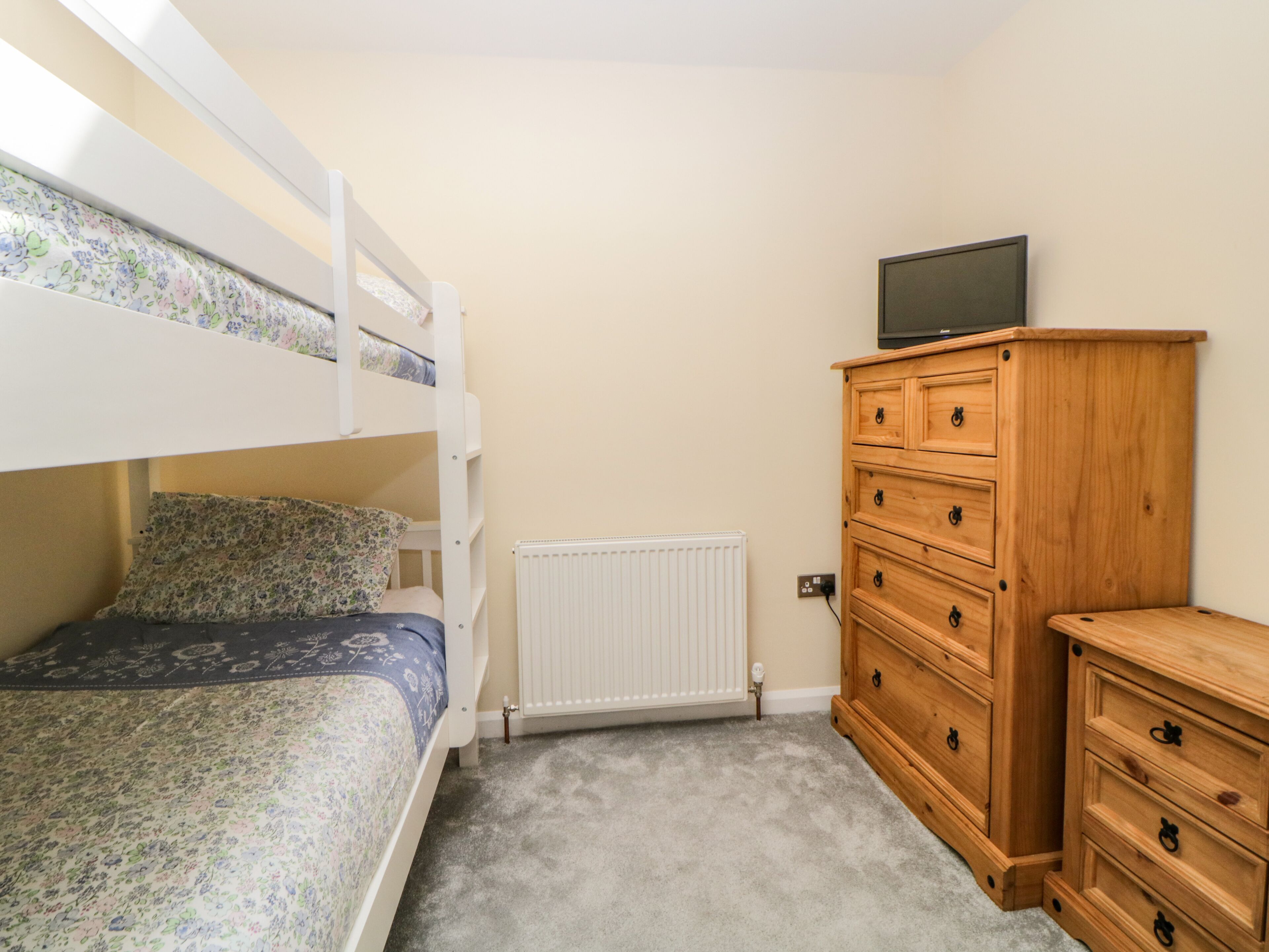A bunk bed with floral bedding, a wooden dresser, and a television on top.