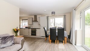 Cocina moderna con armarios blancos y comedor con dos sillas y una mesa.