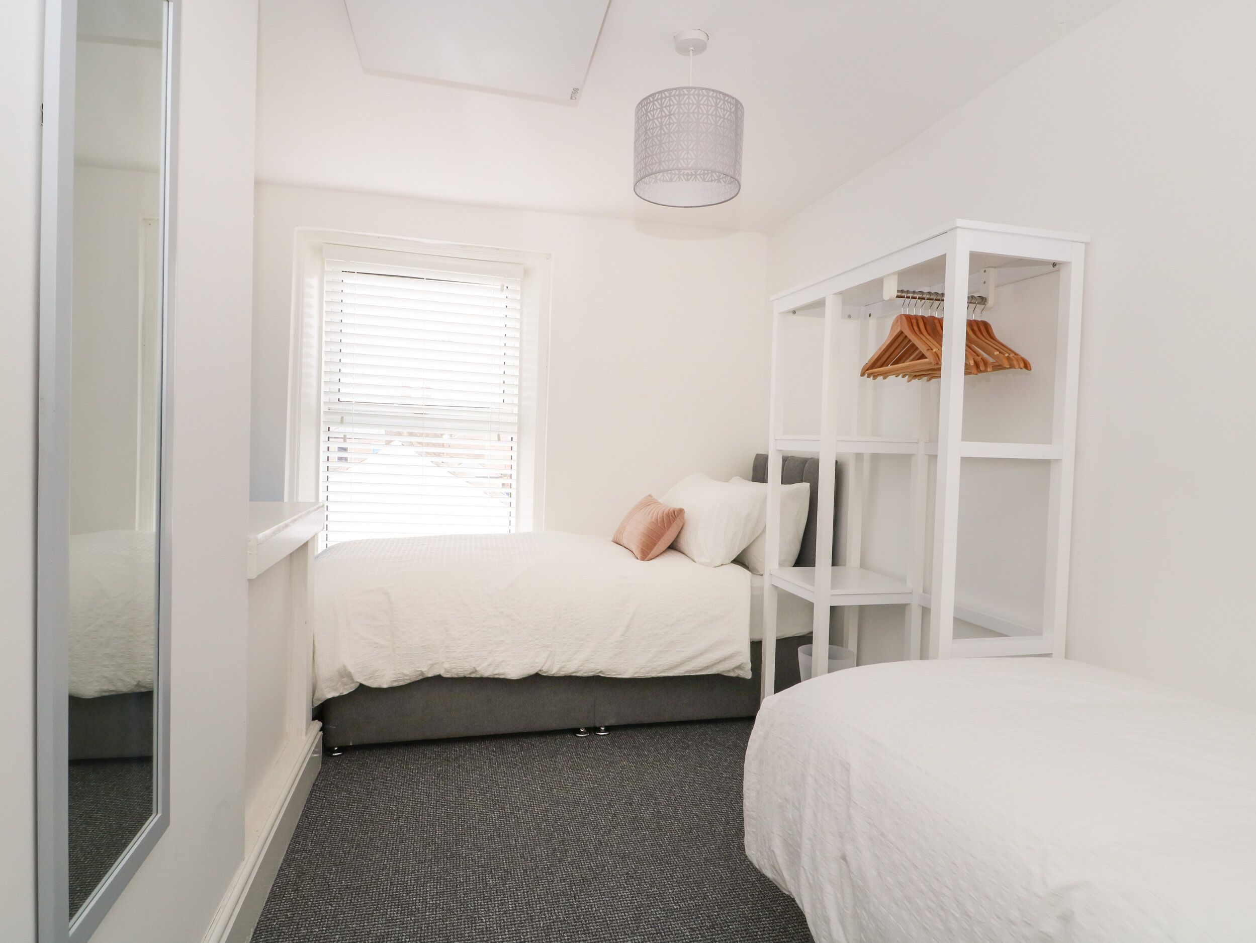 A bedroom with a bed, a wardrobe, a window with blinds, and a hanging light fixture.