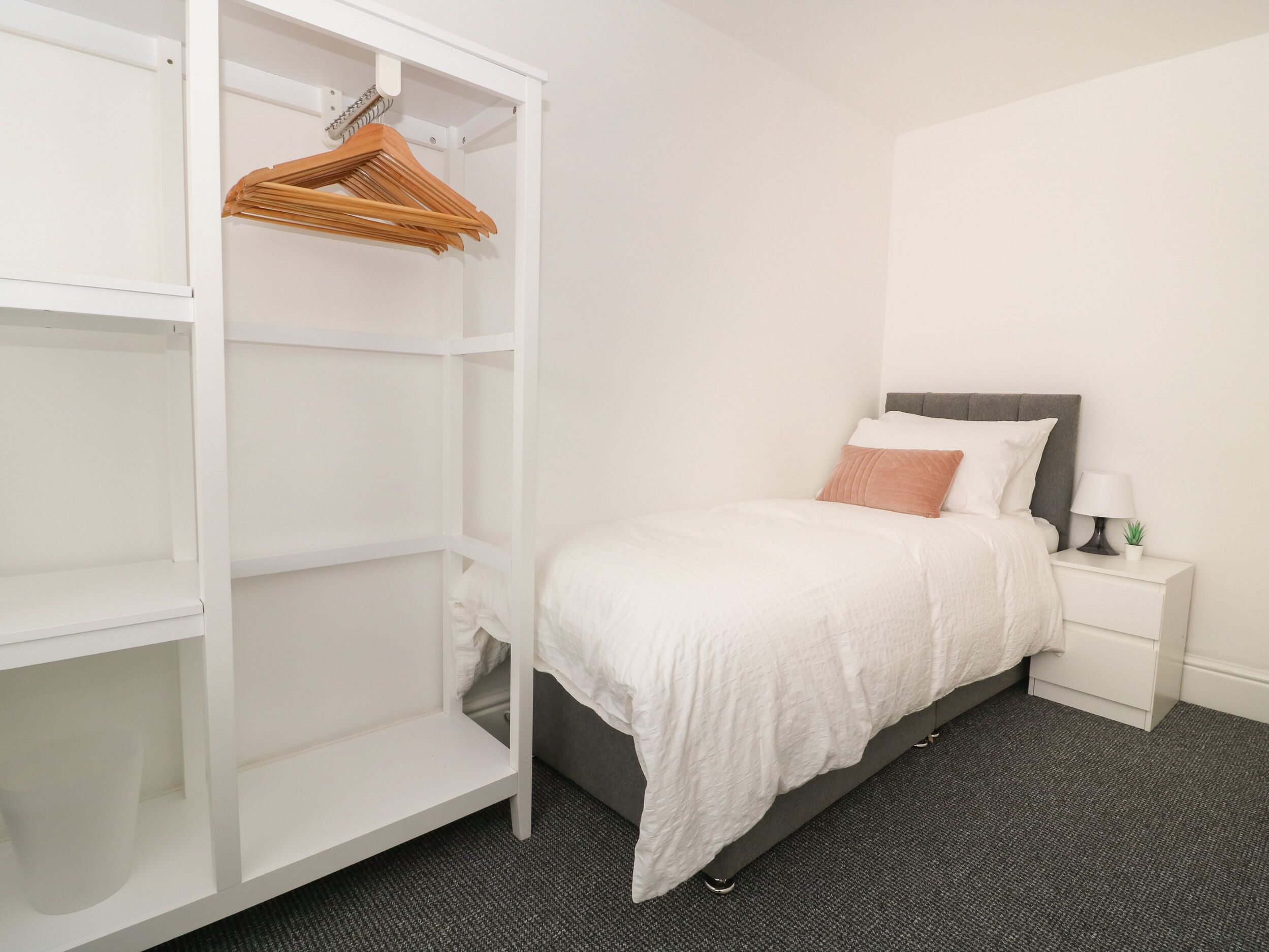 A bedroom with a bed, a nightstand, a white wardrobe, and a wooden hanger.