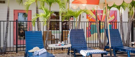 Un patio con sillas reclinables azules, una mesita redonda y un mural colorido en la pared.