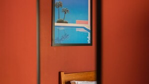 A bedroom with a bed, a nightstand with a lamp, and a framed painting of a beach scene.