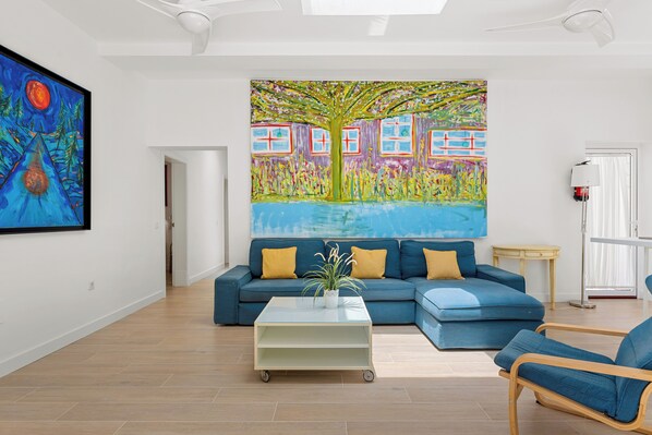 Un salon moderne avec un canapé bleu, une table basse et un tableau abstrait aux couleurs vives accroché au mur.