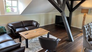 Een loft-achtige woonkamer met een donkere houten vloer, een bruine leren bank, een houten salontafel en een zwarte leren fauteuil.