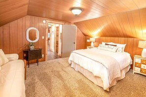 Ein gemütliches Schlafzimmer unter der Schräge mit einem großen Bett, einem Schminktisch, einem Nachttisch und einem Spiegel.