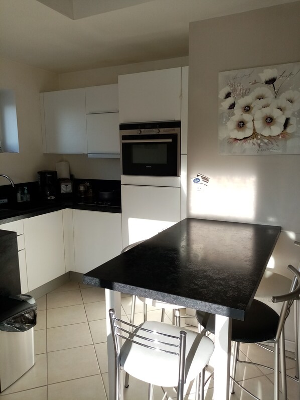 A modern kitchen with white cabinets, a black countertop, and stainless steel appliances. There is a painting of flowers on the wall.