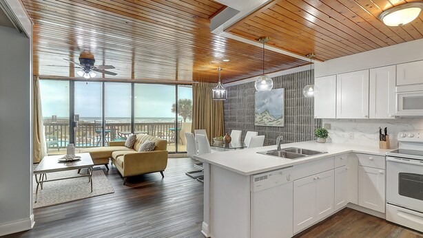 A modern kitchen with white cabinets, a dishwasher, and an oven. There is a large window with a view of the outdoors.