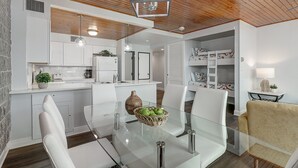 A modern kitchen with white cabinets, a glass dining table, and a wooden ceiling.