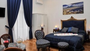 A hotel room with a large bed, a chair, a small table with a glass, and a painting on the wall. - Di Palma Suite Museum (Napoli)