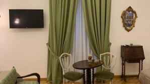 A living room with a wooden floor, a TV mounted on the wall, a dining table with chairs, and a sofa. - Di Palma Suite Museum (Napoli)