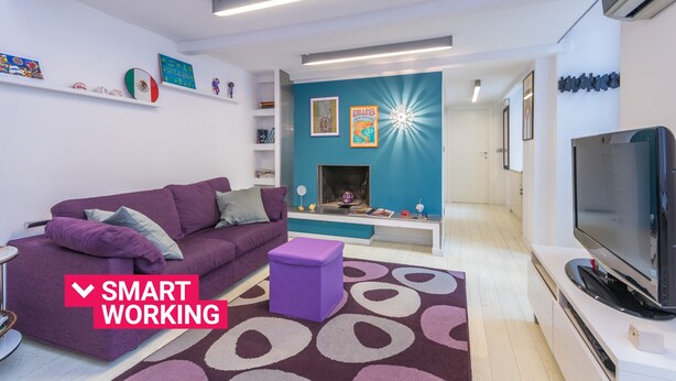 Una sala de estar moderna con un sofá morado, un pequeño taburete morado, un televisor de pantalla plana y una chimenea.