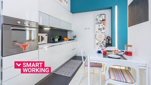 Una cocina moderna con armarios blancos, un horno de acero inoxidable y una zona de comedor con una mesa y sillas blancas.