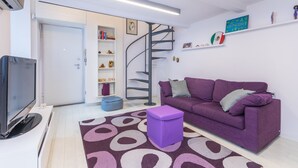 Una sala de estar moderna con un sofá púrpura, un televisor de pantalla plana, una escalera espiral y una estantería.