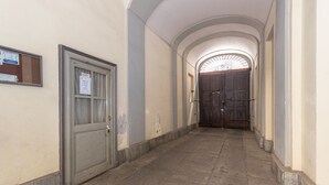Un pasillo con una puerta cerrada a la izquierda, una ventana con un aviso y un gran portón de madera al final.