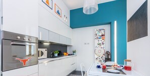 A modern kitchen with white cabinets, a stainless steel oven, and a dining area with a white table and chairs. - Pura Vida Duplex by Wonderful Italy (Torino)