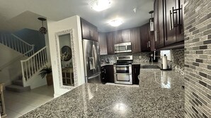 A modern kitchen with granite countertops, stainless steel appliances, and dark wooden cabinets. - US Open Pickleball Stay - 3 Masters - Walkable Location (Naples)